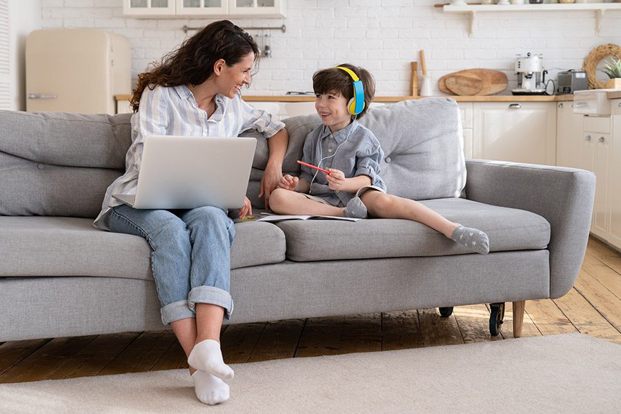 Client Center - Happy Mother Using Laptop is Laughing With Son While he Wears Headphones at Home