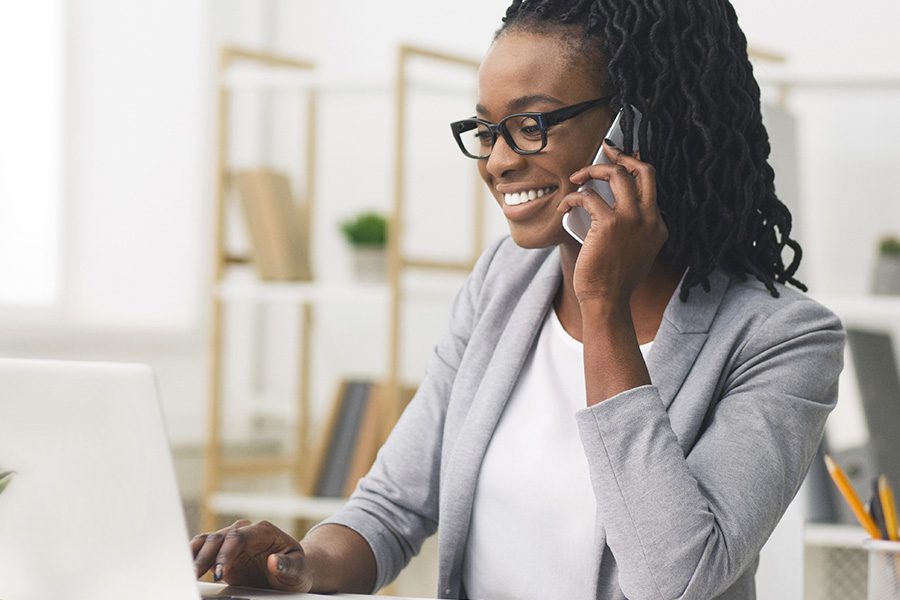 Contact - Smiling Woman on Phone Using a Laptop at Her Office